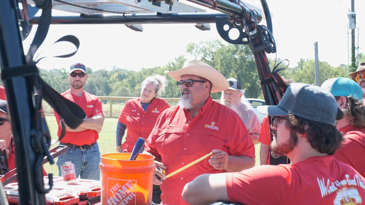 Crew in red company shirts gathered at the back of a work truck, a bucket and hand tools between them.