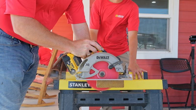 A Bell crew member cutting a board with a cordless circular saw on a portable workbench