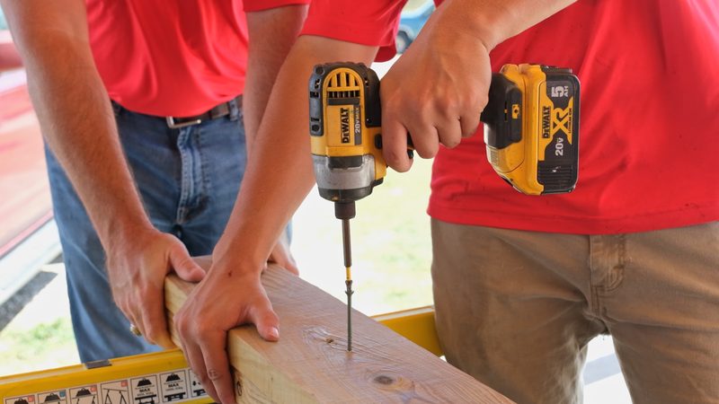 Driving a screw into a board with a cordless impact driver while a second crew member holds it steady
