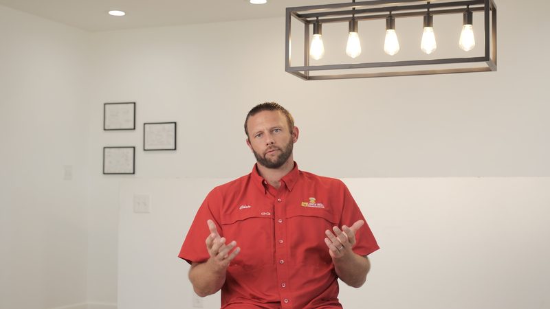 A member of the Bell team in a red company shirt, seated indoors and talking with both hands raised.