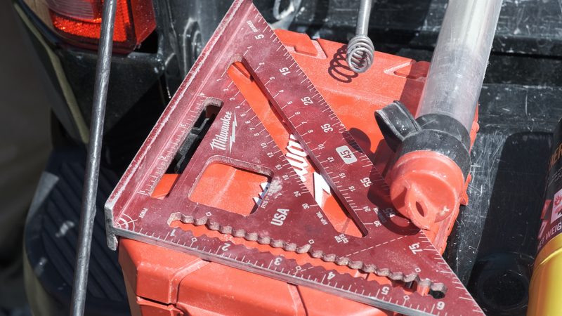 A speed square, a hammer and a length of pipe on a tool box in the bed of a Bell work truck