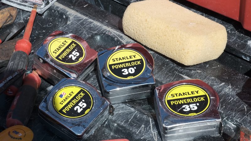 Four tape measures, screwdrivers and a sponge laid out on a truck tailgate